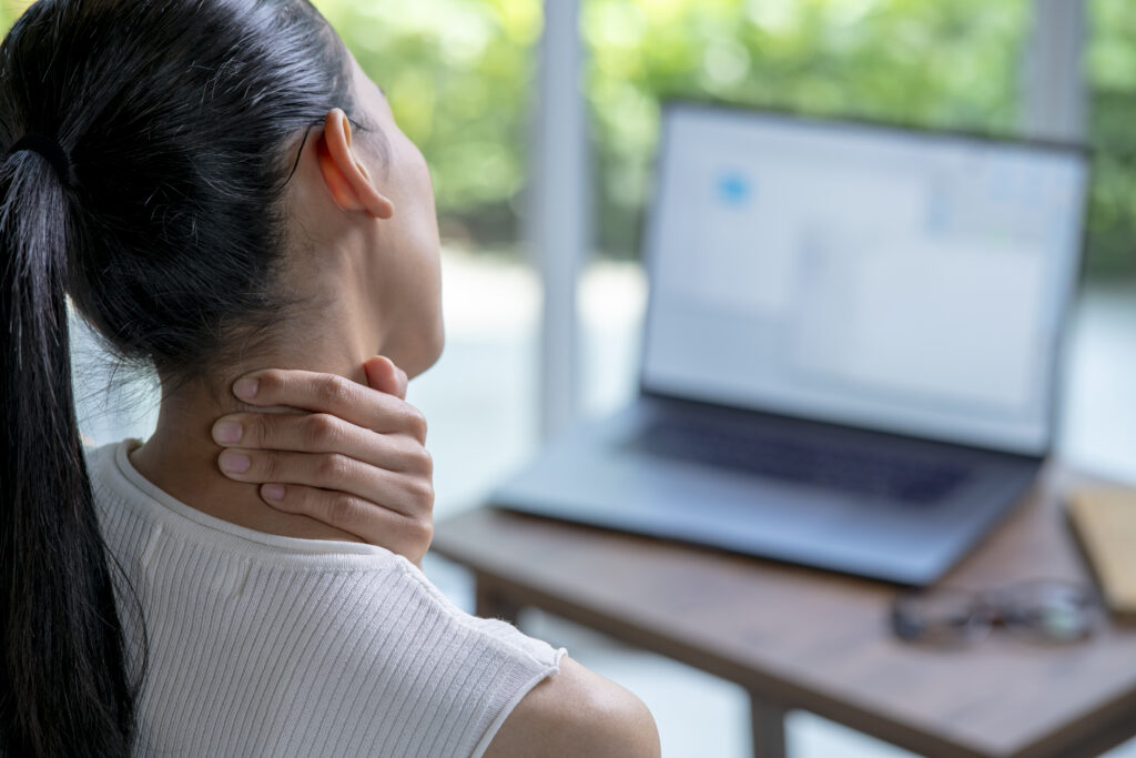 Desk worker with neck pain from screens rubbing the back of their neck